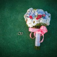 Обручальные кольца и букет невесты из голубых гортензий, белых эустом и ярко-розовых роз, украшенный белой и розовой атласной лентой