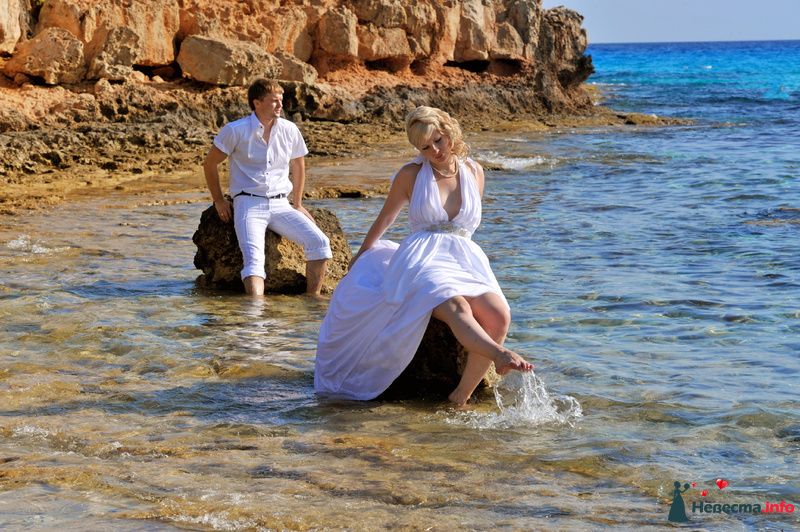 Жених в белой рубашке и шортах сидит на камне омываемом водой, впереди на таком же камне невеста в белом платье - фото 148198 Honey)))