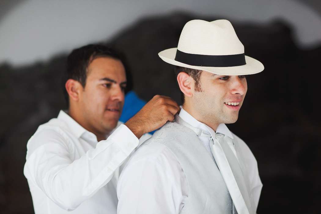 Жених в белой рубашке,белой жилетке, белом галстуке и в белой шляпе с черной лентой - фото 1159755 Exclusivaweddings - организация свадьбы на Санторини