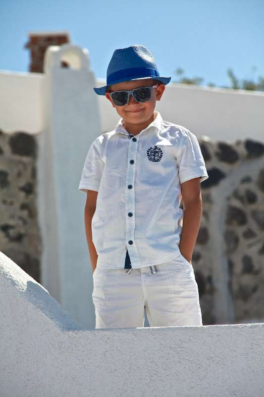 Мальчик в летний солнечный день в белой рубашке со светлыми штанами,  в голубой красивой шляпе и солнцезащитных очках - фото 1848659 Exclusivaweddings - организация свадьбы на Санторини
