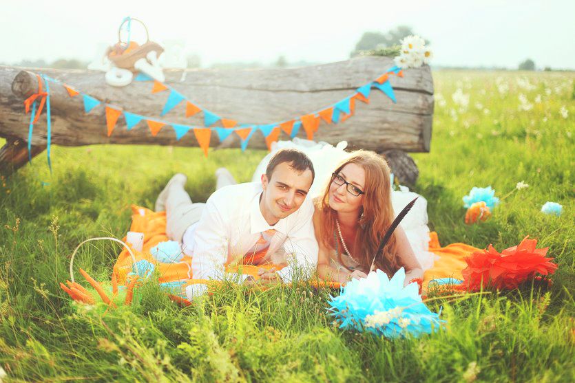 В поле возле полена, украшенного гирляндой из голубых и оранжевых флажков лежат на траве жених и невеста - фото 1283681 Фотограф Юлия Леденёва