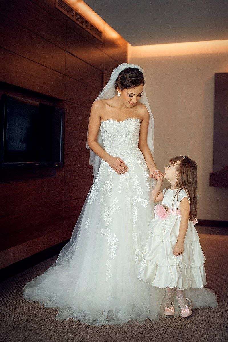Маленькая девочка в белом пышном платье ,в комнате у телевизора , стоит рядом с невестой и держит ее за руку - фото 1617583 ElegantMoment - Свадьба в Дубае и ОАЭ