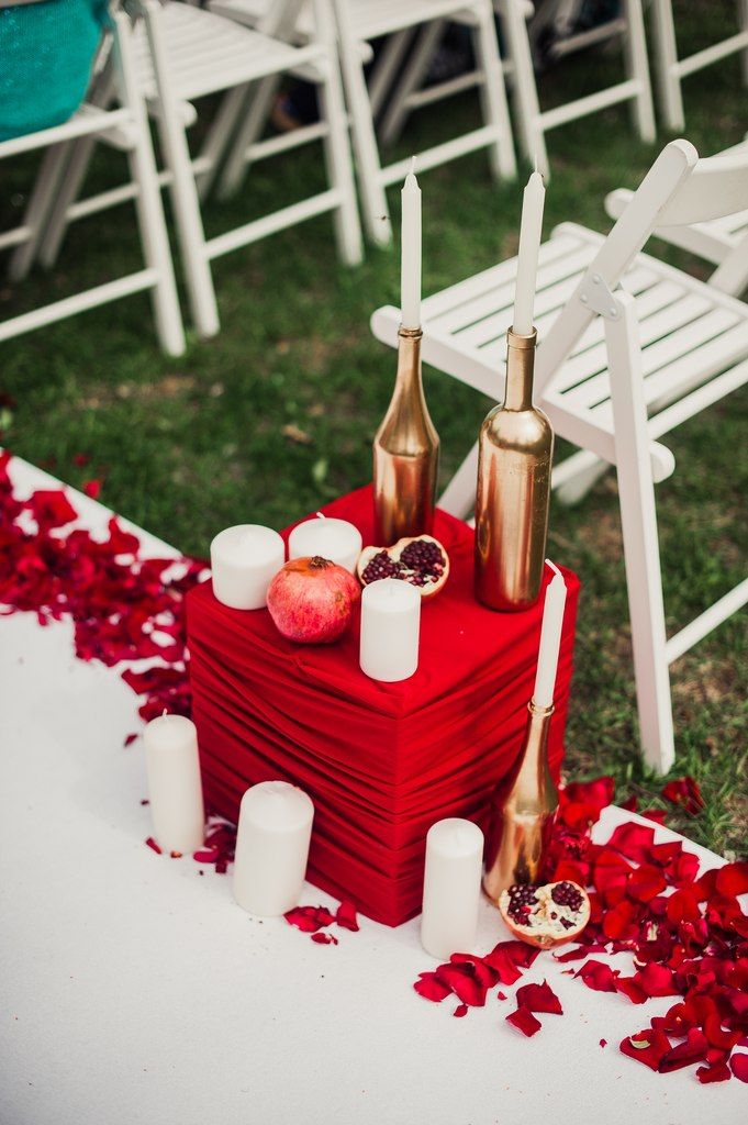 Подсвечники в виде позолоченных бутылок и белых свечей и гранат, на фоне красного куба - фото 2430441 "Honey Honey Decor" декор событий