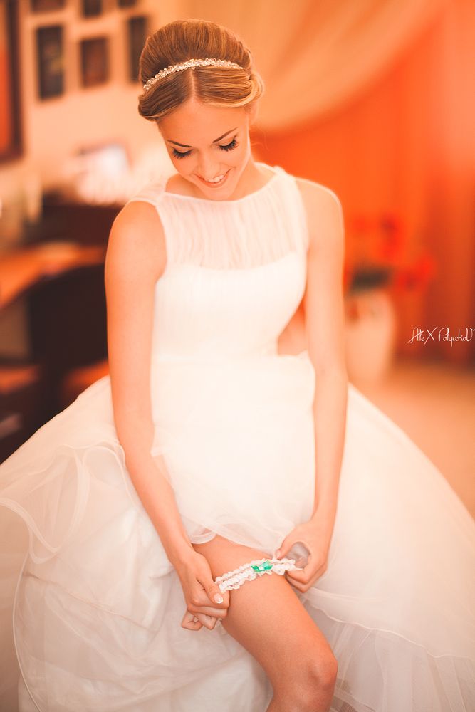 Невеста одевает на ногу белую кружевную подвязку с голубым атласным бантом - фото 2513189 Свадебный Фотограф Александр Поляков