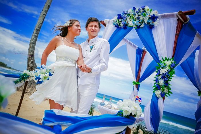 Возле свадебного шатра, украшенного в белых и голубых тонах стоят молодожены, жених в белых брюках и рубашке держит за руку  - фото 733179 Свадебное агентство "Свадьба-Недорого"