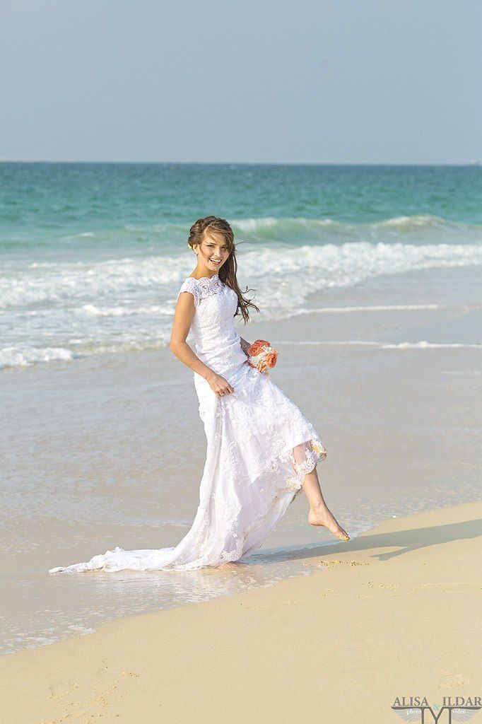 На побережье тропического пляжа стоит счастливая невеста в белом ажурном платье, она кокетливо приподняла подол юбки, обнажив - фото 2766663 "Tytprod" - фото и видеосъёмка 