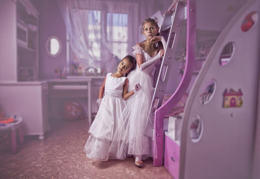 Девочки в белых длинных пышных платьях стоят у кровати в красивой сиреневой детской комнате - фото 1385157 Свадебный фотограф Евгений Иванов
