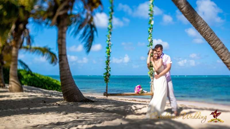 На лазурном побережье возле качели стоят молодожены, жених в светлых брюках и розовой рубашке обнимает за талию невесту в - фото 3418471 Caribbean Wedding - свадьба в Доминикане