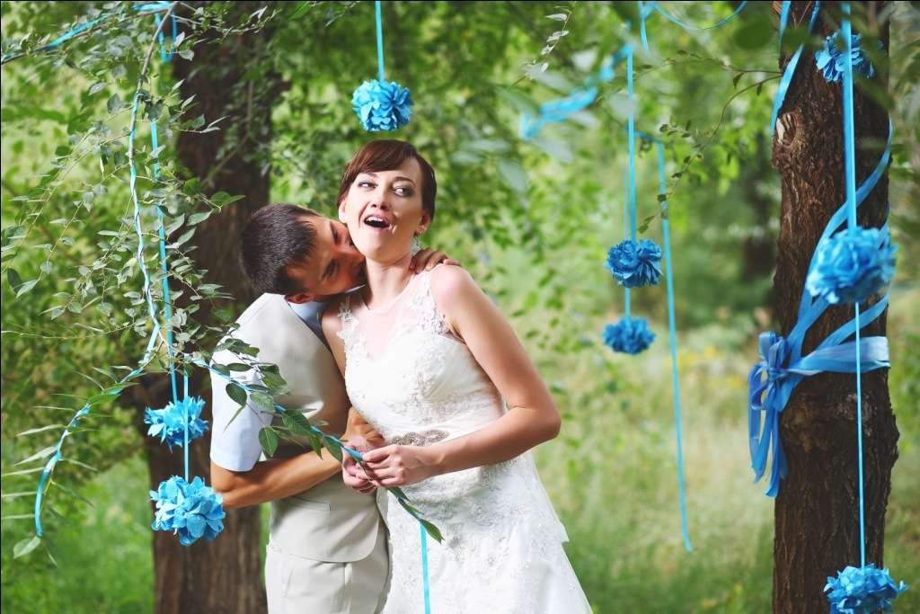 Жених и невеста стоят на фоне деревьев, украшенных голубыми шарами - фото 1401197 Ликусик